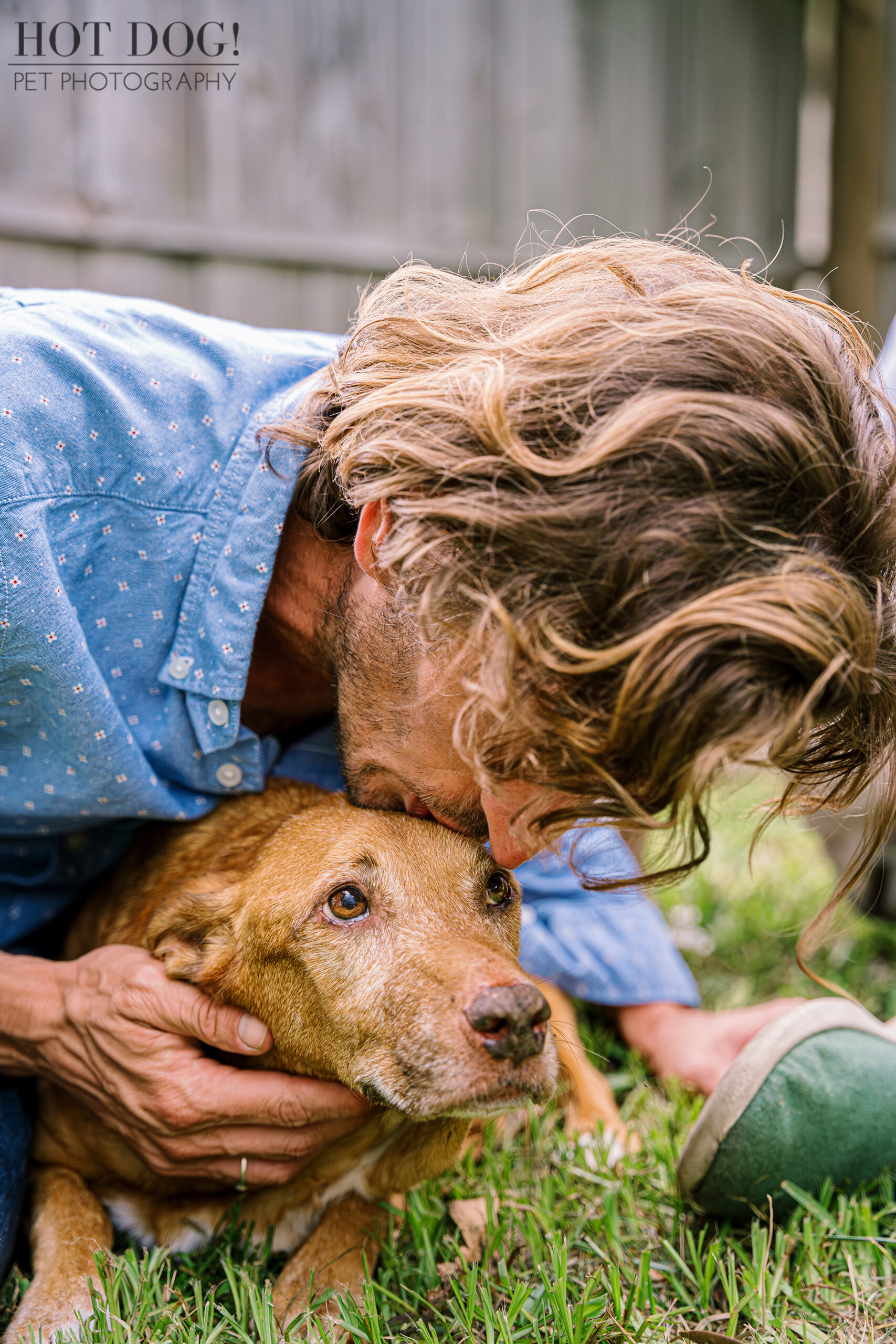 Adelaide, a terminally ill dog, sits calmly on the grass while her dad gently kisses her head. Photo by Hot Dog! Pet Photography.